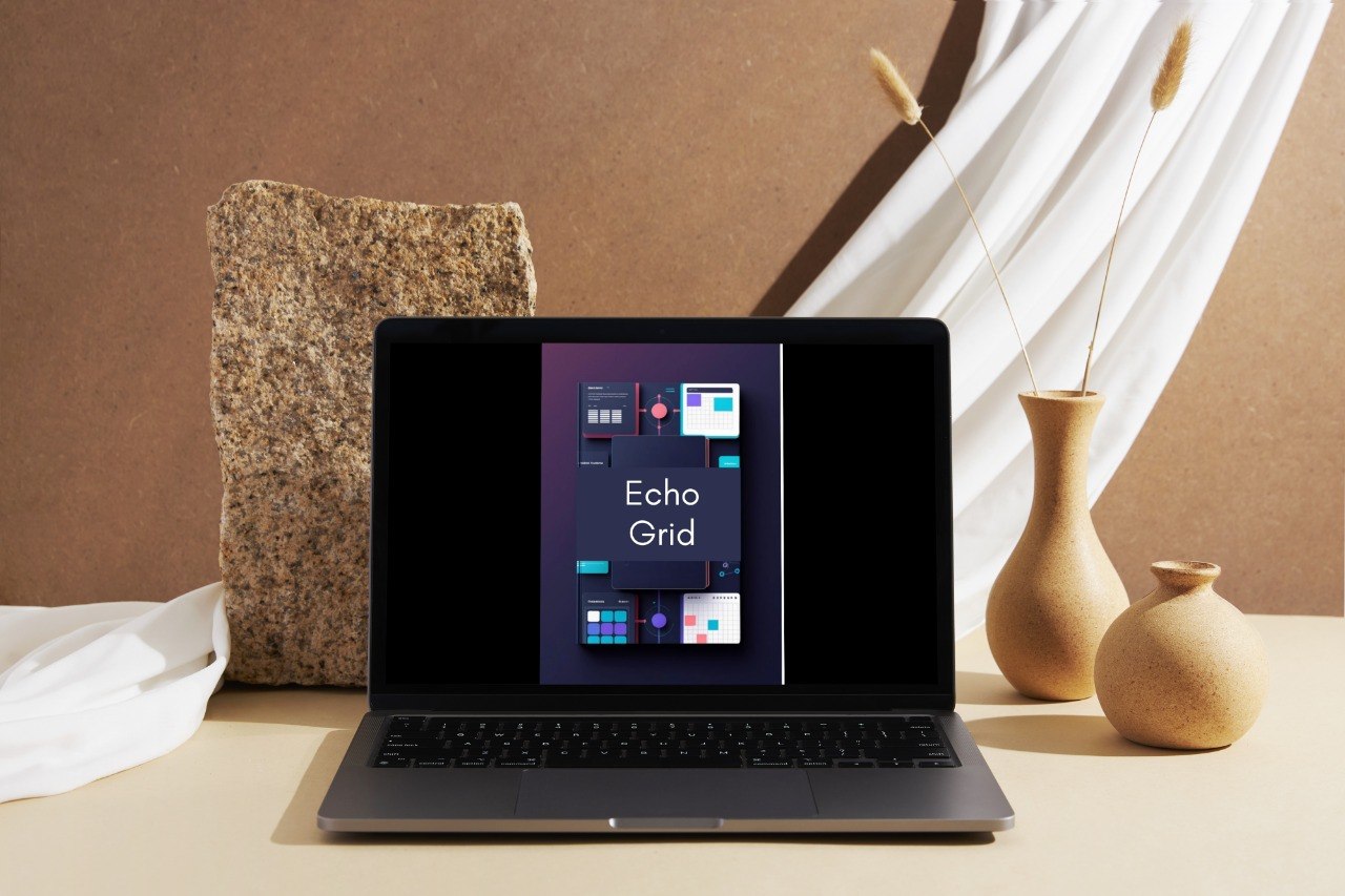 A dark gray laptop sits open on a beige tabletop, displaying the Windows 11 Start screen with the Echo Grid app. The setup is styled with a textured stone block, white draped fabric, and two beige ceramic vases in the background.